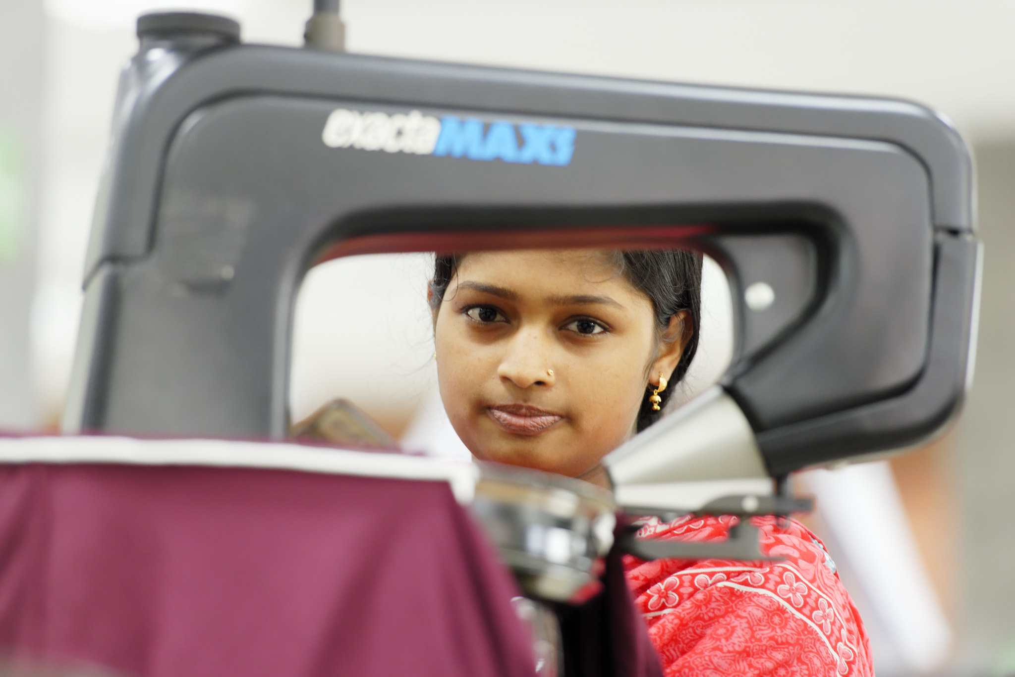 Một phụ nữ trẻ người Bangladesh mặc đồ đỏ ngồi sau chiếc máy may.