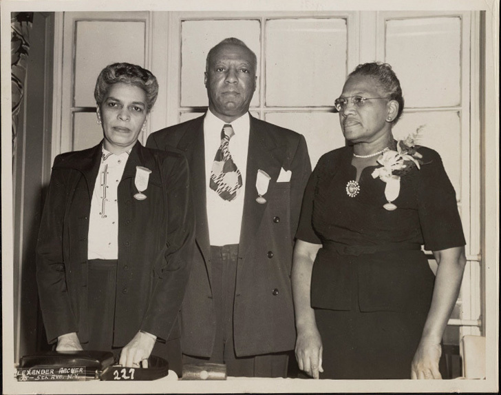 Black and white photo of Rosina Tucker standing with A. Philip Randolph and Helena Wilson. All are dressed formally, with a medal pinned to their jackets.
