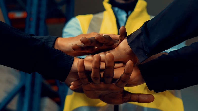 A pair of hands overlapping with each other with an individual in the background with a yellow vest. 