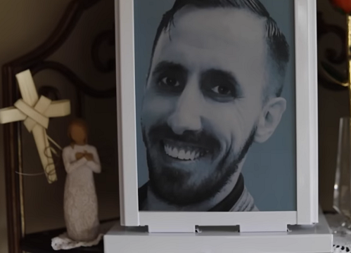A cross and a carved wooden angel sit next to a framed black and white photo of Timothy Barber.