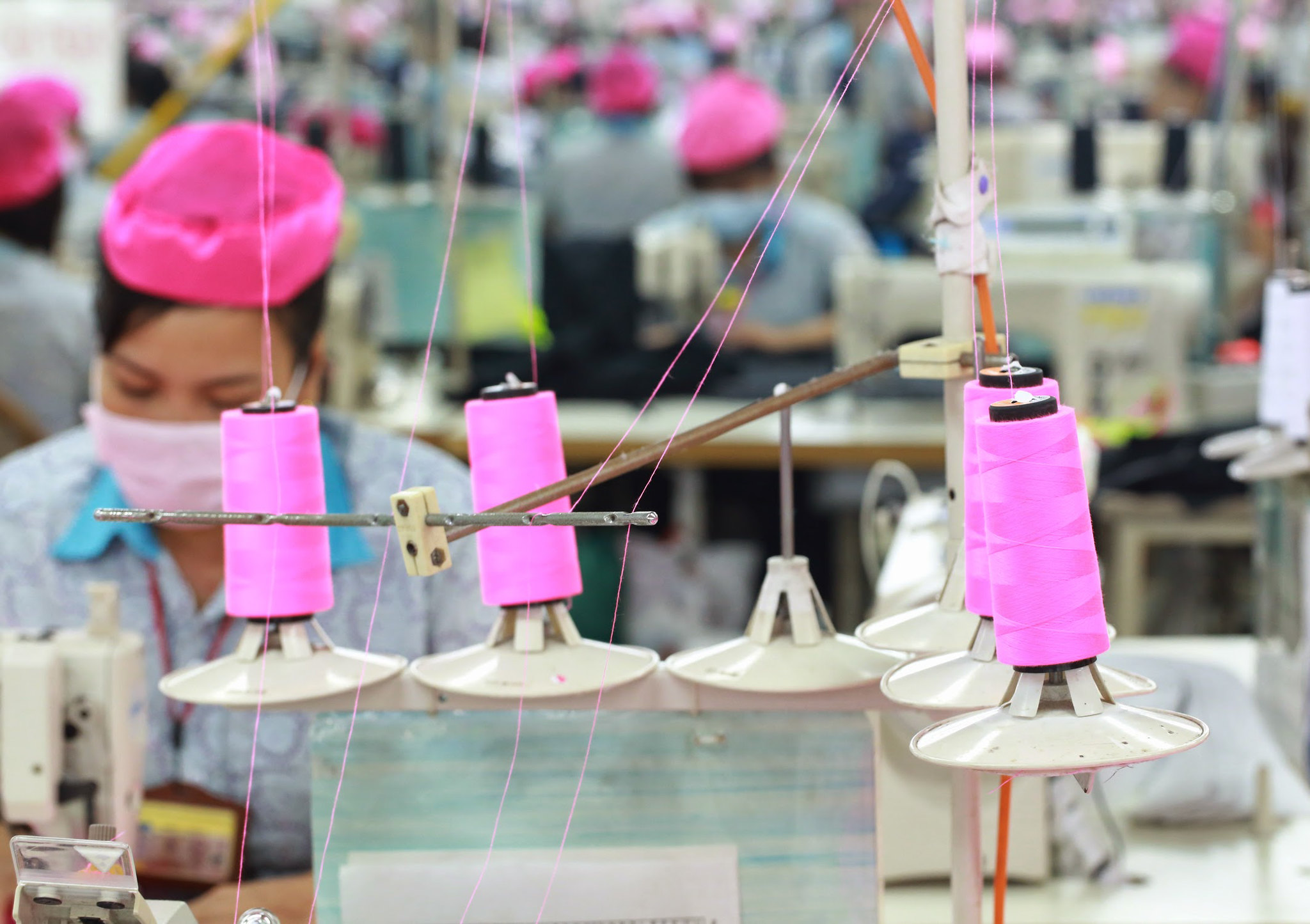 A garment worker at a Better Work factory in Vietnam. Spools of pink thread are visible in the foreground. Credit: Better Work.