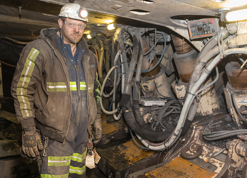 A coal miner covered in dust works inside an underground mine.