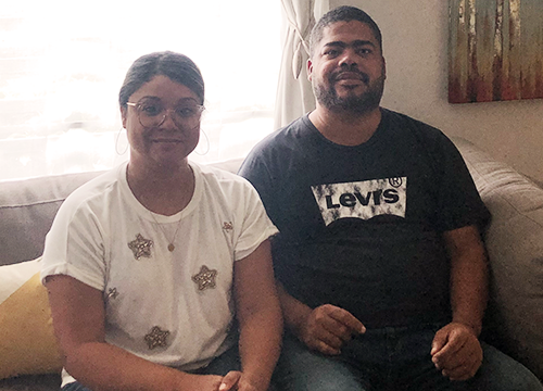 A man and a woman sit on a couch in a living room.