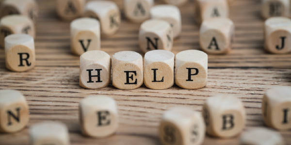 Small alphabet blocks are scattered across a table. In the center, four blocks spell out the word “help.”