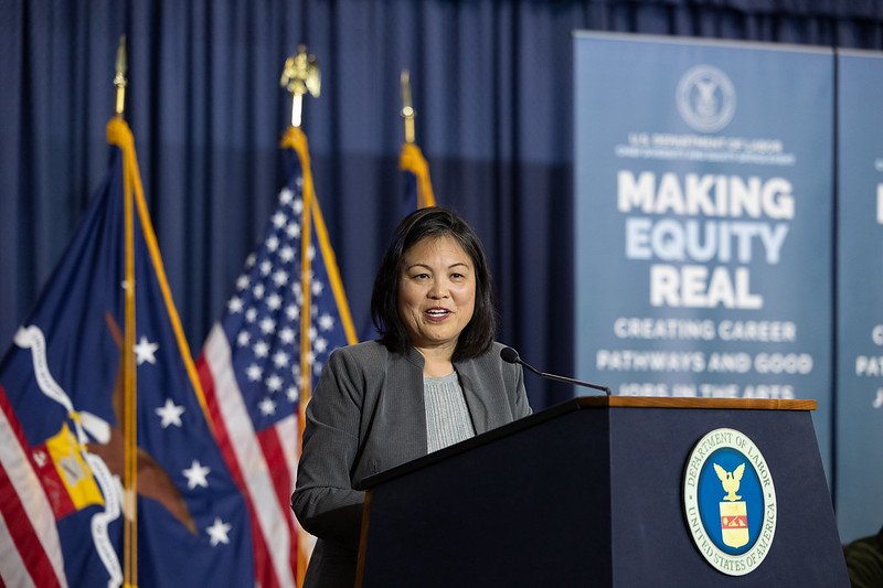 Acting Secretary Julie Su giving a speech at a podium with a sign that says "making equity real" in the background.