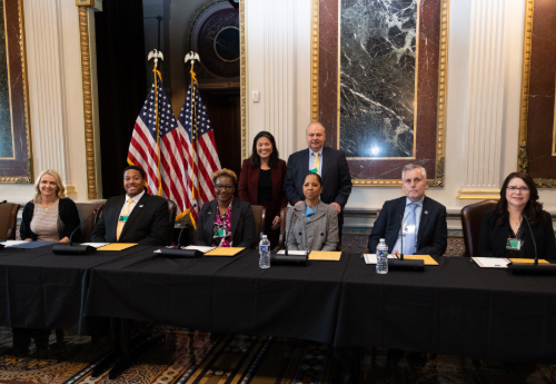 John Ladd stands next to Acting Secretary Su behind six panelists at the 2024 Cybersecurity Apprenticeship Event.