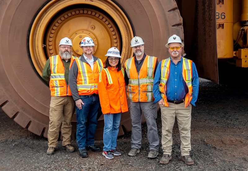 Acting Secretary of Labor Julie Su and Assistant Secretary of Labor for Mine Safety and Health Chris Williamson stand with three MSHA staff members in front of a large vehicle tire. 