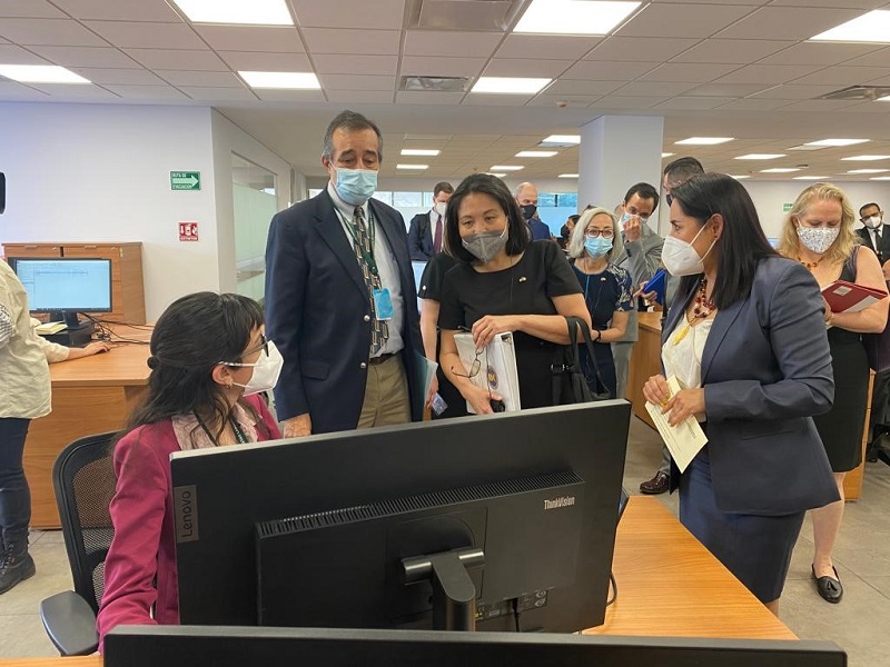  Julie Su standing next to the Director of the Federal Center, Dominguez Marrufo, looking at a worker's computer screen in the Federal Center offices.