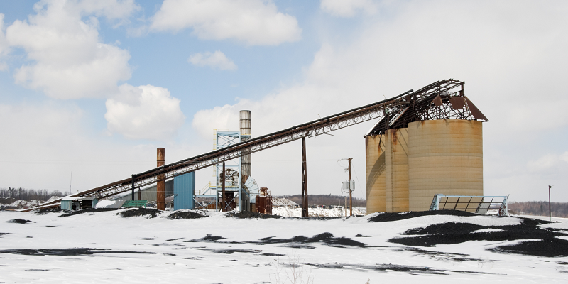 A light snowfall blankets surface equipment at a mine, including silos and a conveyor system.