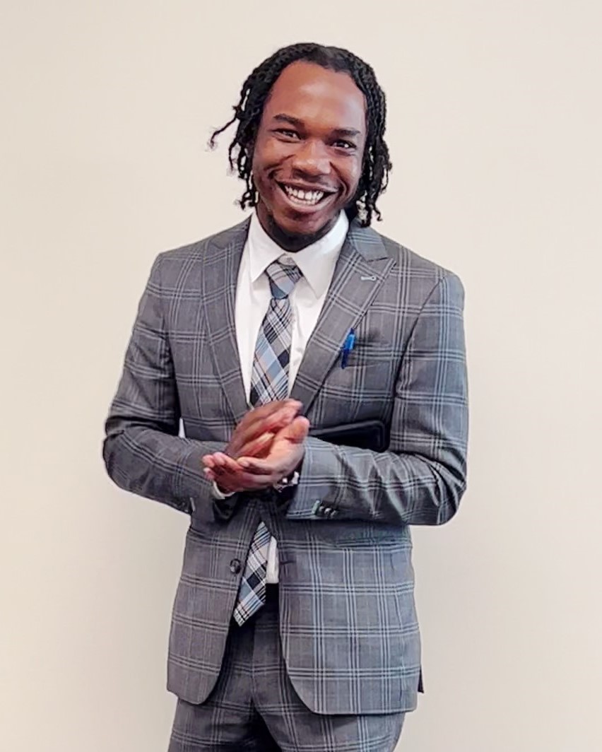 Photo of Tajay Kelly standing in a grey suit and smiling