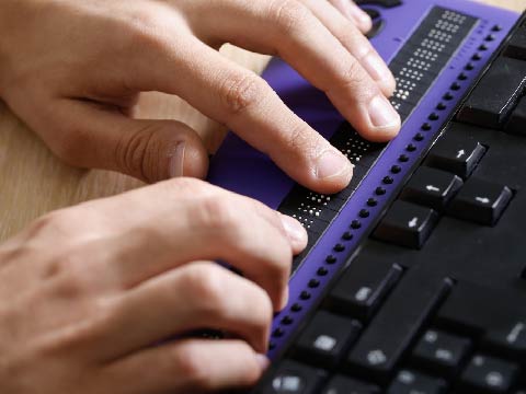 Close-up of hands typing on a braille keyboard