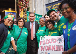 Secretary Walsh with a group of diverse union workers who are wearing green shirts. One carries a sign that says "Proud Worker."