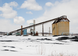 A light snowfall blankets surface equipment at a mine, including silos and a conveyor system.