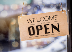 A sign hangs in a shop window that says "welcome, we are open, please come in"
