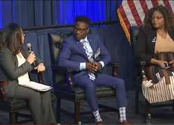 Three people in professional clothes sit on a stage, having a panel conversation. 