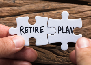 Two white puzzle pieces being held together by male hands with the words "retire" and "plan" written in black on the two pieces. 