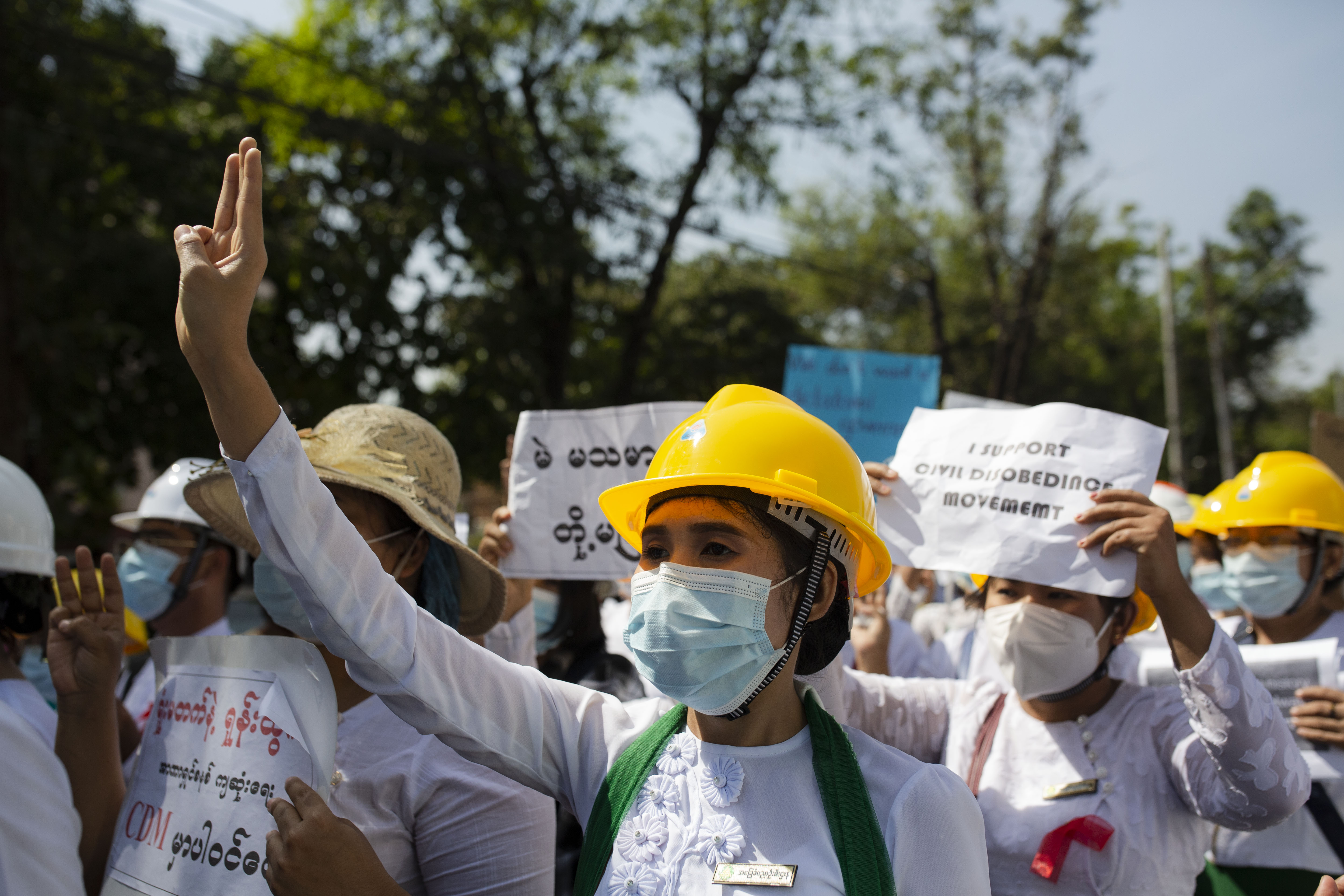 Workers wearing white clothing and face masks protest in Myanmar. Many are holding signs.