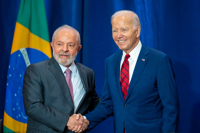 President Biden shaking hands with President Lula in front of the Brazilian flag. 