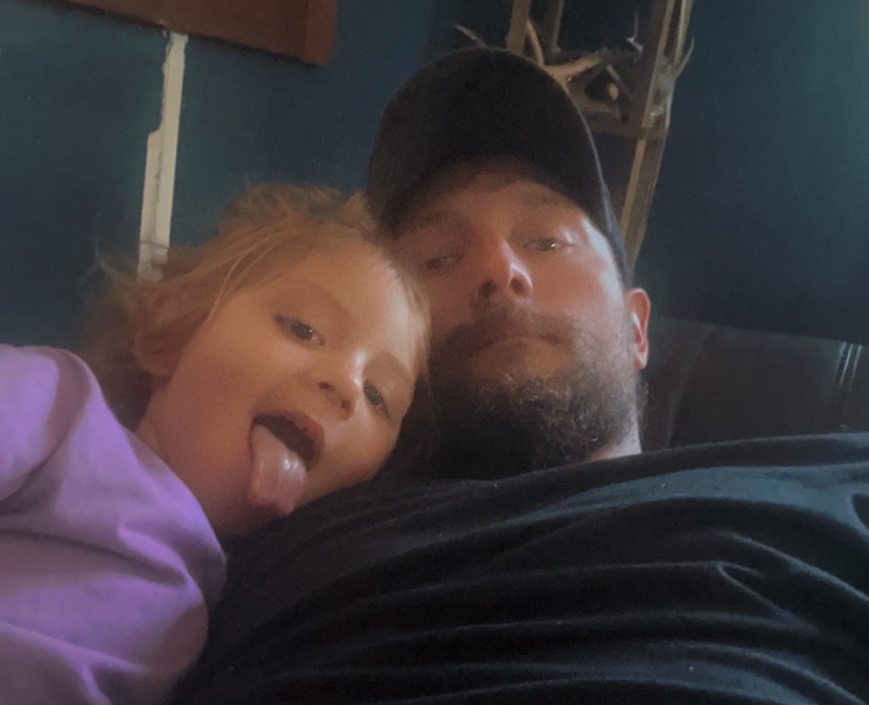 Kevin and his young daughter take a selfie. She is making a silly face.