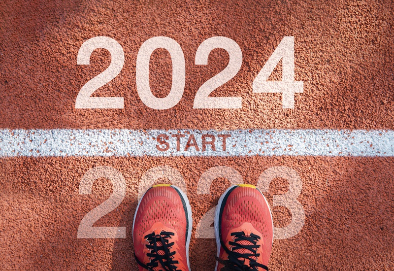 A person wearing running shoes looks down at their feet. They stand on a starting line between 2023 and 2024 written on the ground.