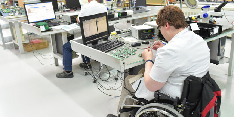 A worker who uses a wheelchair at a workplace in a electronics manufacturing and assembly factory