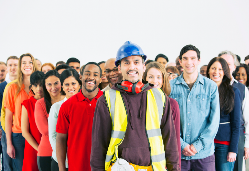 一名男子戴着安全帽、耳罩和反光背心，站在一群微笑的工人面前。 