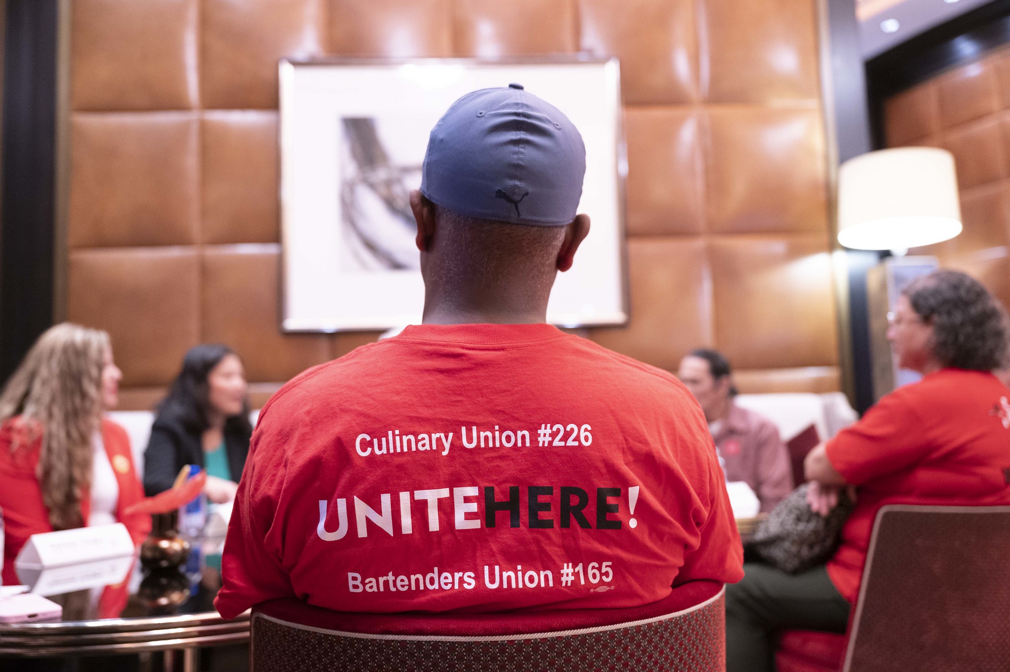 Several workers sit and talk with Acting Secretary Su at The Venetian Resort. One worker’s red shirt, seen from the back, has the words “Culinary Union #226. Unite Here! Bartenders Union #165.” 