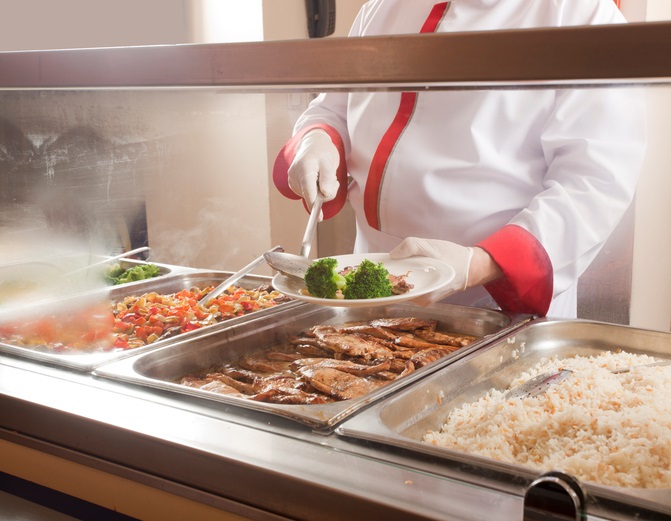 A cafeteria worker places food on a tray.
