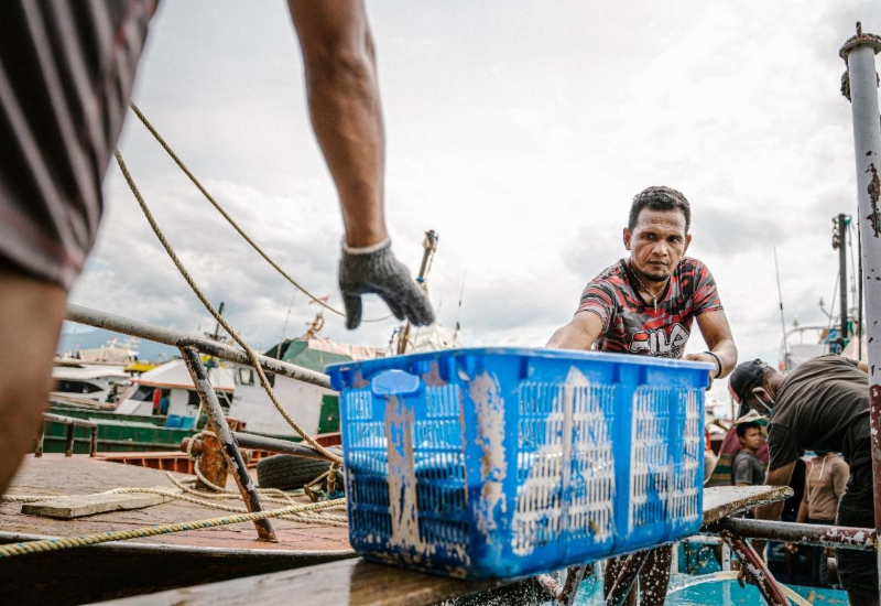 Fishers handling a large blue crate on a dock in Thailand.