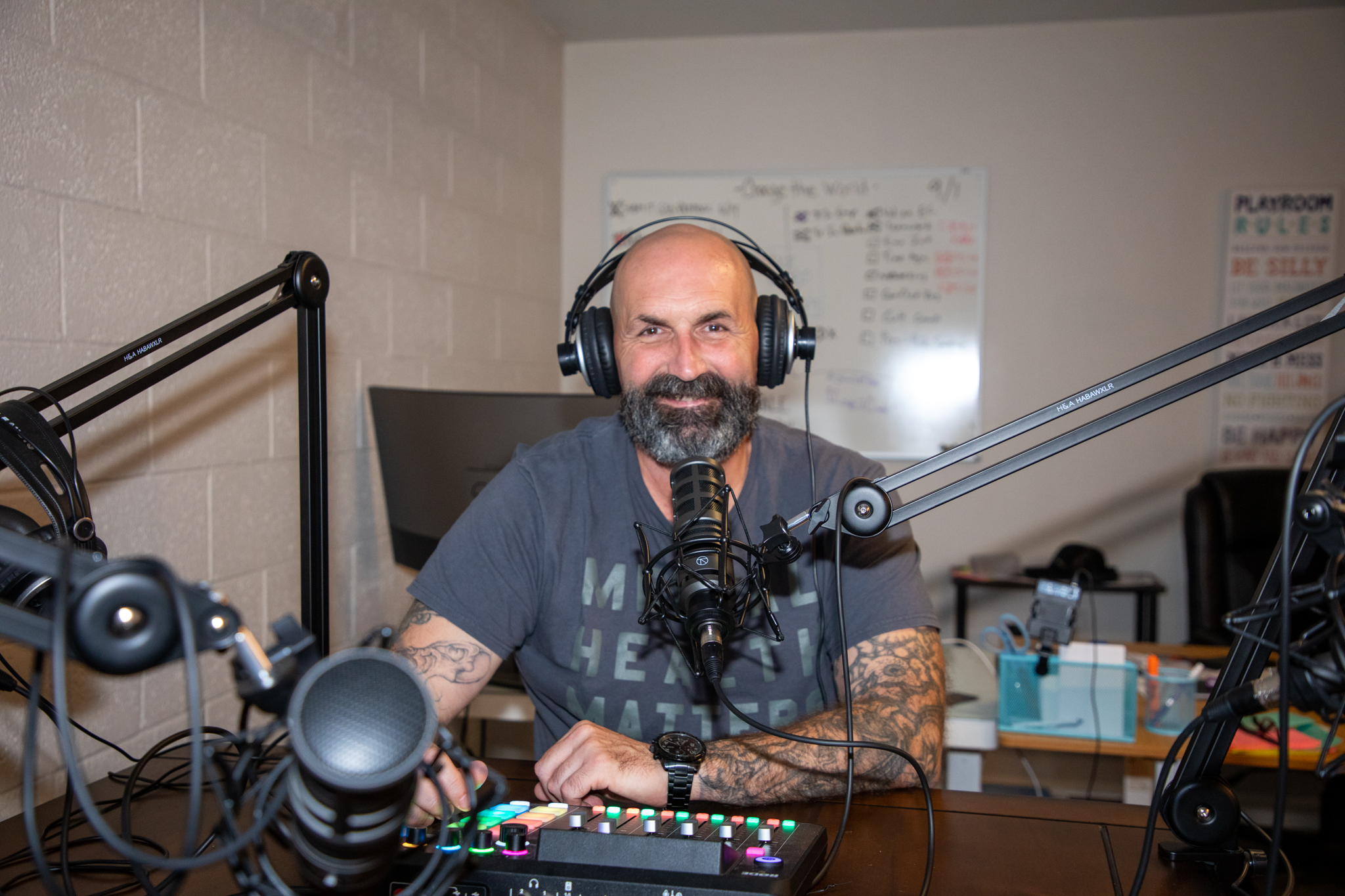 George Nolan sits at a desk wearing headphones with a recording microphone near his mouth. 