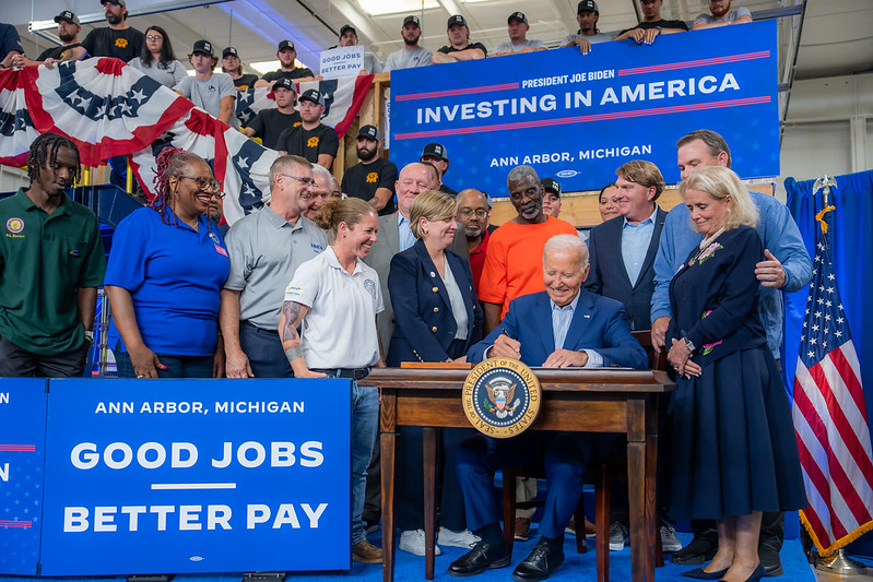 President Joe Biden, flanked by union members and labor leaders, signs an Executive Order to promote good jobs. Signs around him say "Investing in America" and "Good jobs, better pay." (Official White House Photo by Adam Schultz) 