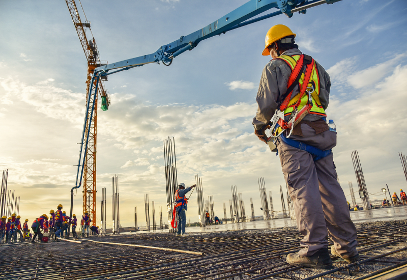 A construction worker in safety gear stands beneath a crane on a construction site.