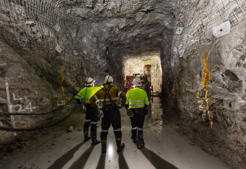 Three mine workers in an underground mine. All are wearing helmets and reflective gear.