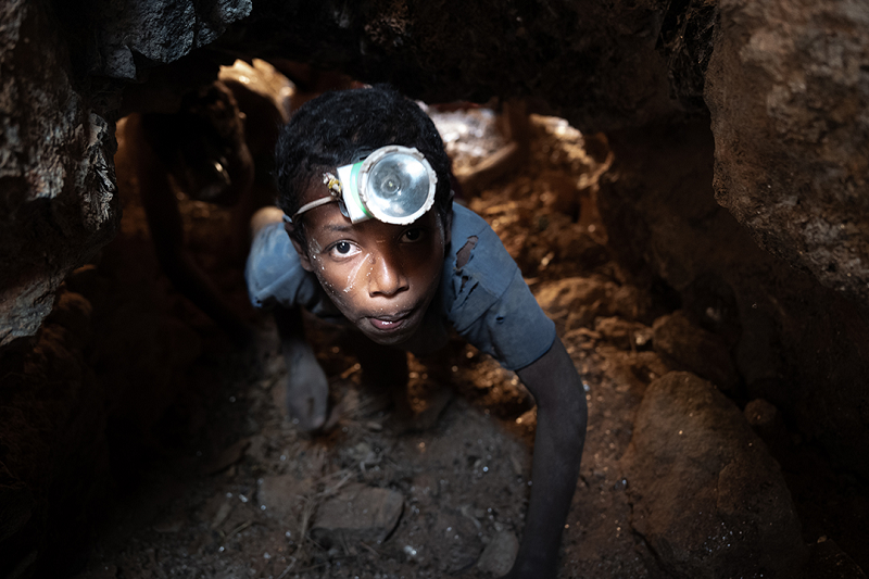 A boy wearing a headlamp works underground in a mica mine.