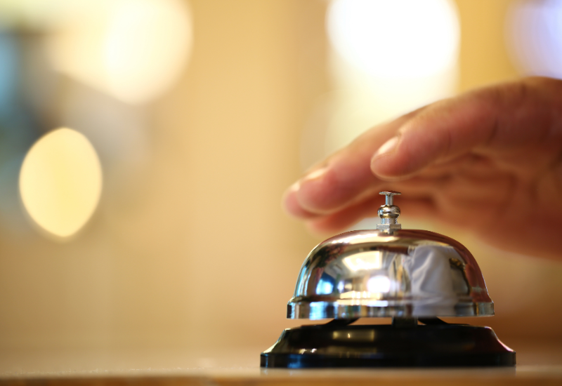 A hand ringing a bell on a hotel desk.