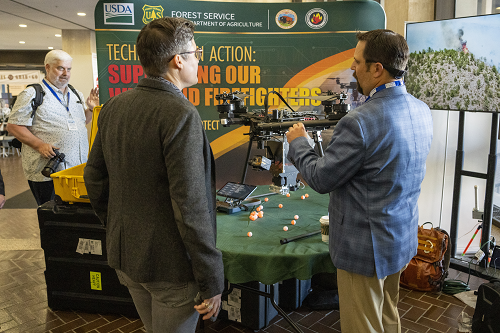 A Forest Service representative shows an event attendee a drone that sits on a table.