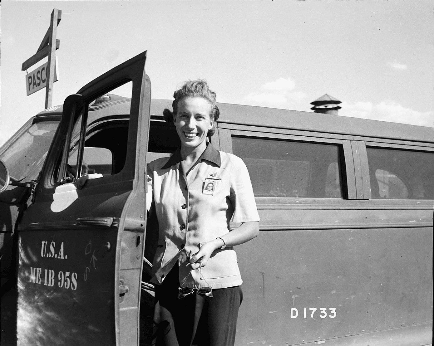 Black and white 1940s photo of a woman standing next to a government-issue truck she drives.