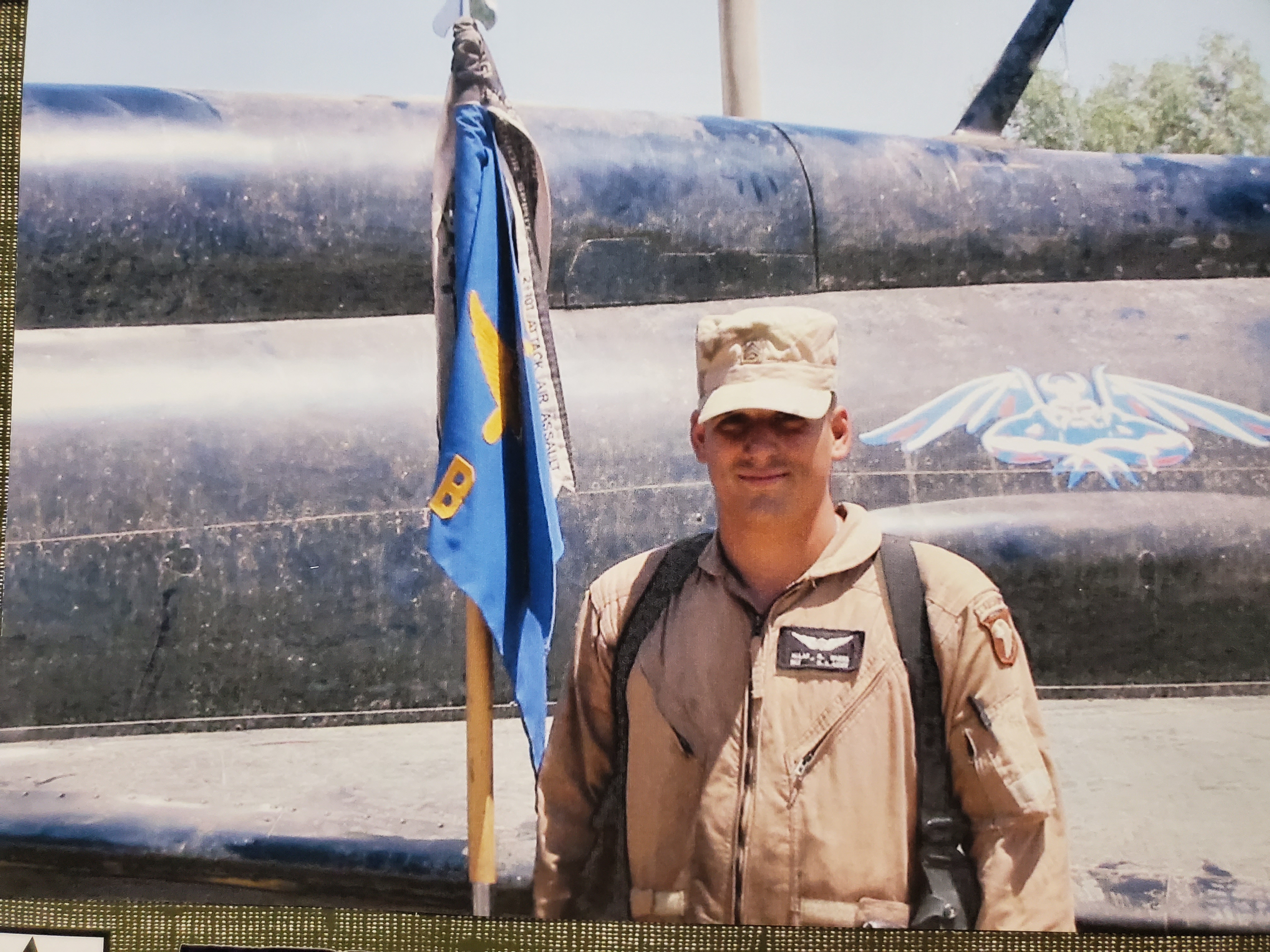 A military veteran in combat gear stands next to a military plane.