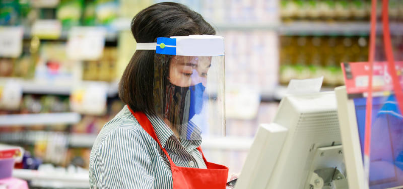 A cashier works at a grocery store wearing protective equipment to prevent viral transmission.