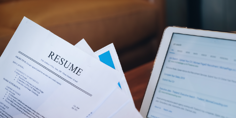 A stack of resumes fanned out in front of a computer