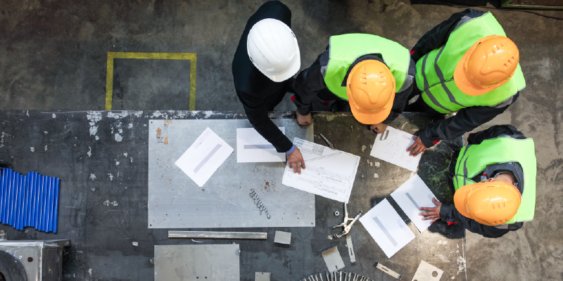 A group of construction workers stand around a table looking at blueprints