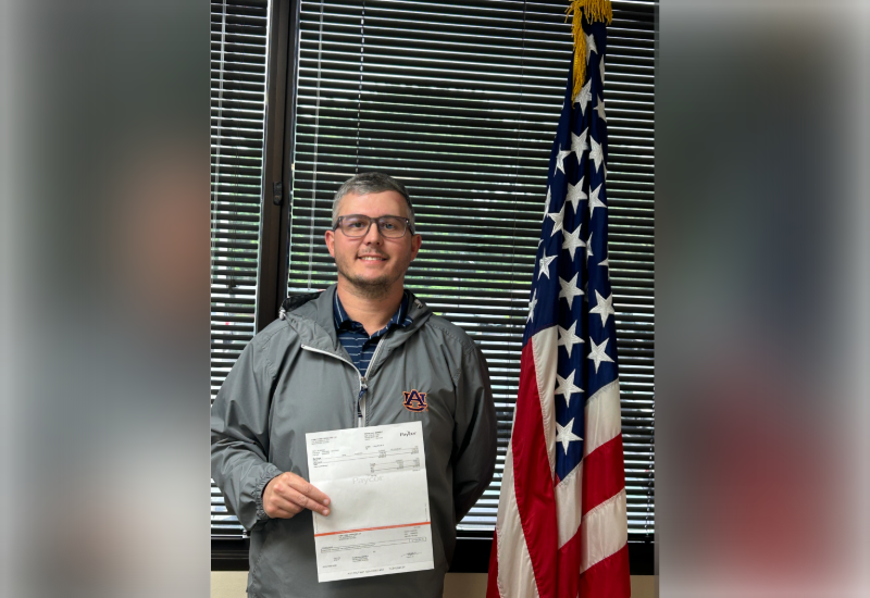 Man posing with a check next to American flag. 