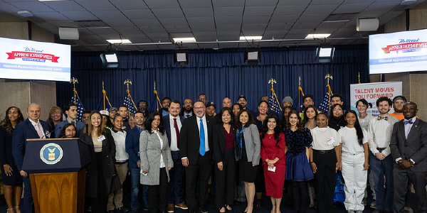 Secretary Su, Secretary Cardona, government officials, students and others crowd together on a stage for a group photo.