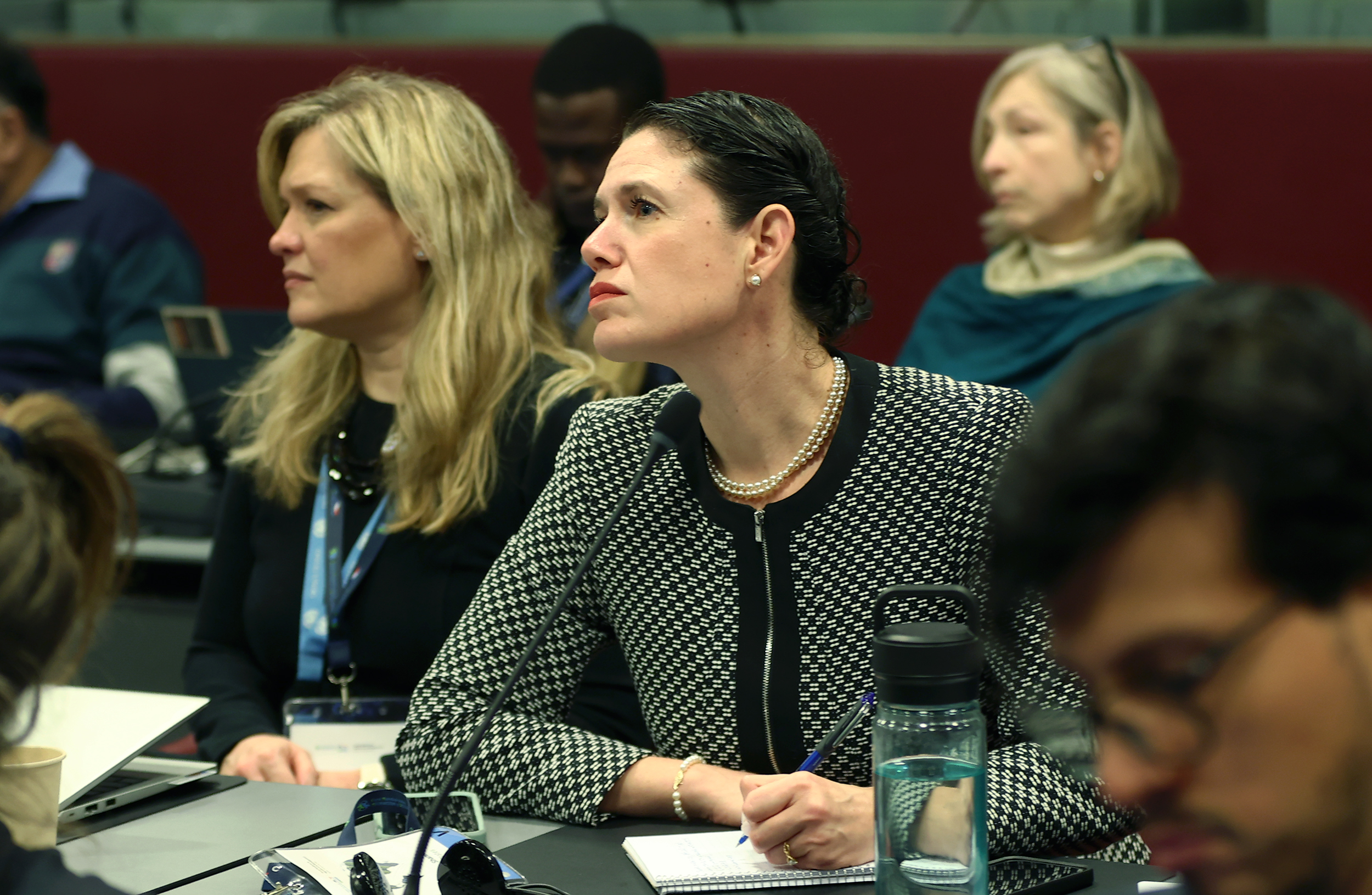 A woman with dark hair wearing a black and white jacket listens intently during a panel discussion.
