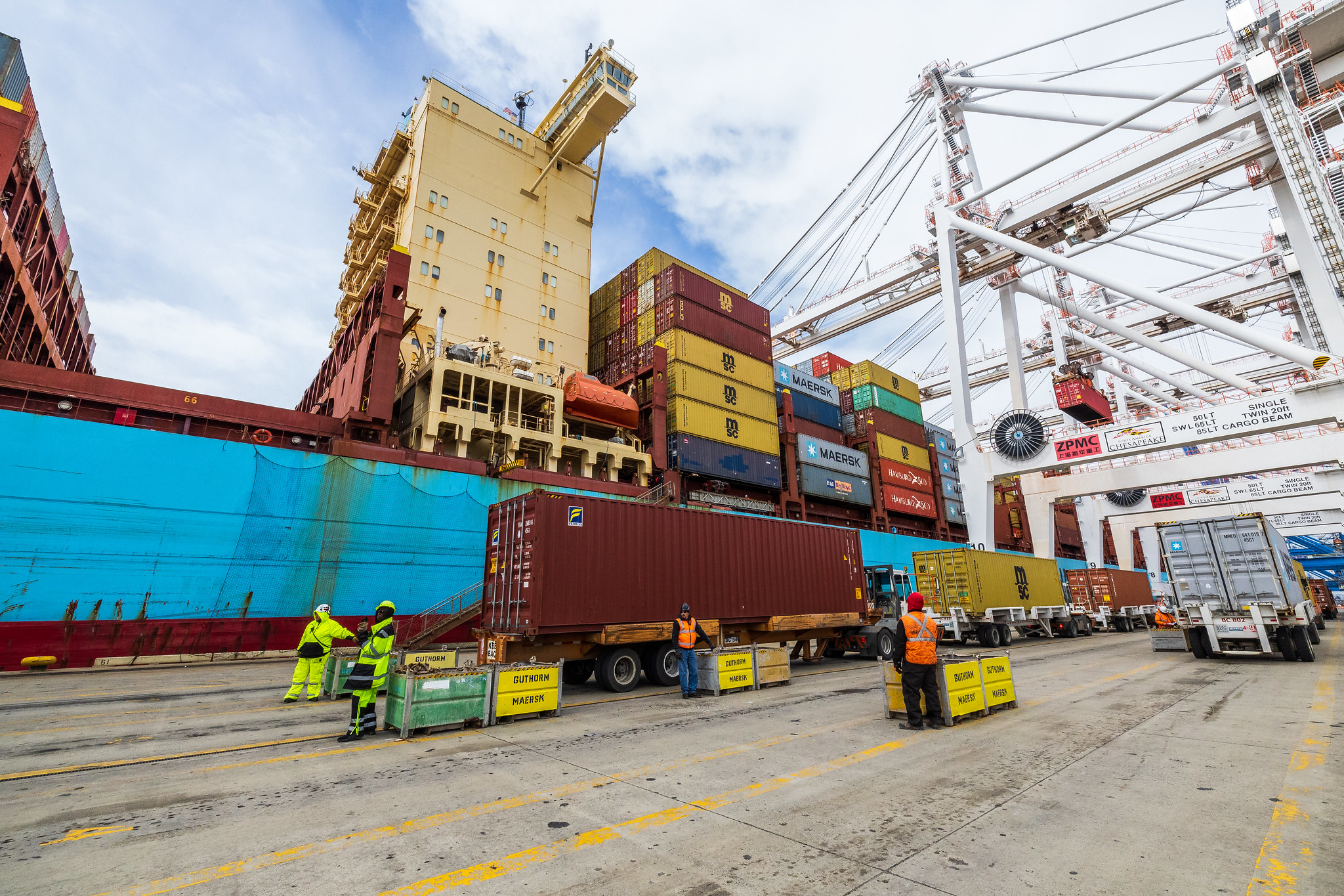 Several workers unload cargo from large containers at a port.