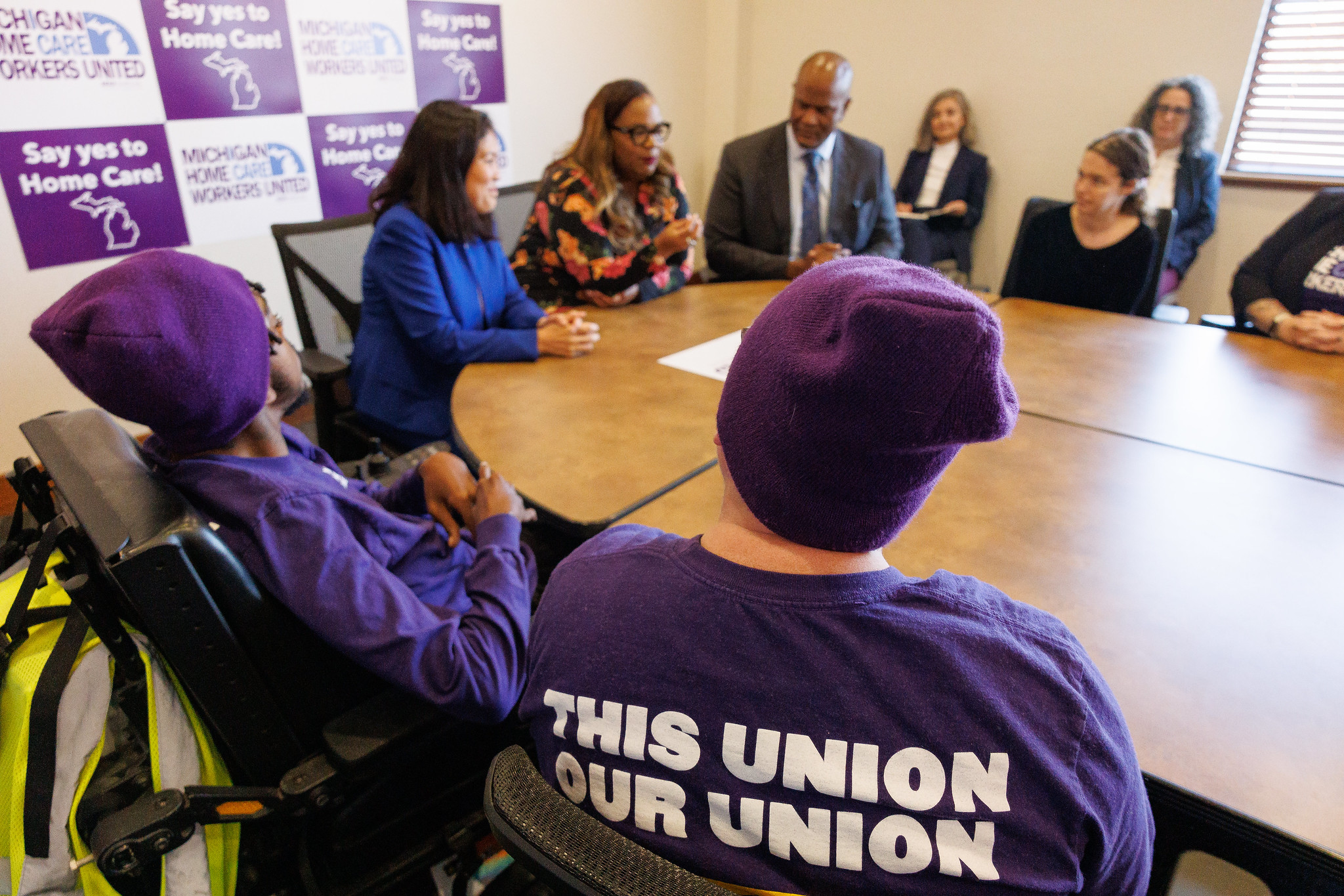 Acting Secretary Su sits around a table with a group of workers wearing purple and local leaders. The back of one worker’s shirt says, “This union, our union.” A banner behind her reads, “Say yes to Home care!” and “Michigan Home Care Workers United.”