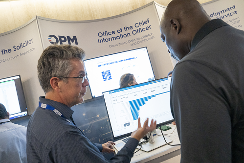 An OPM representative talks about a bar chart on a computer monitor with an event attendee.