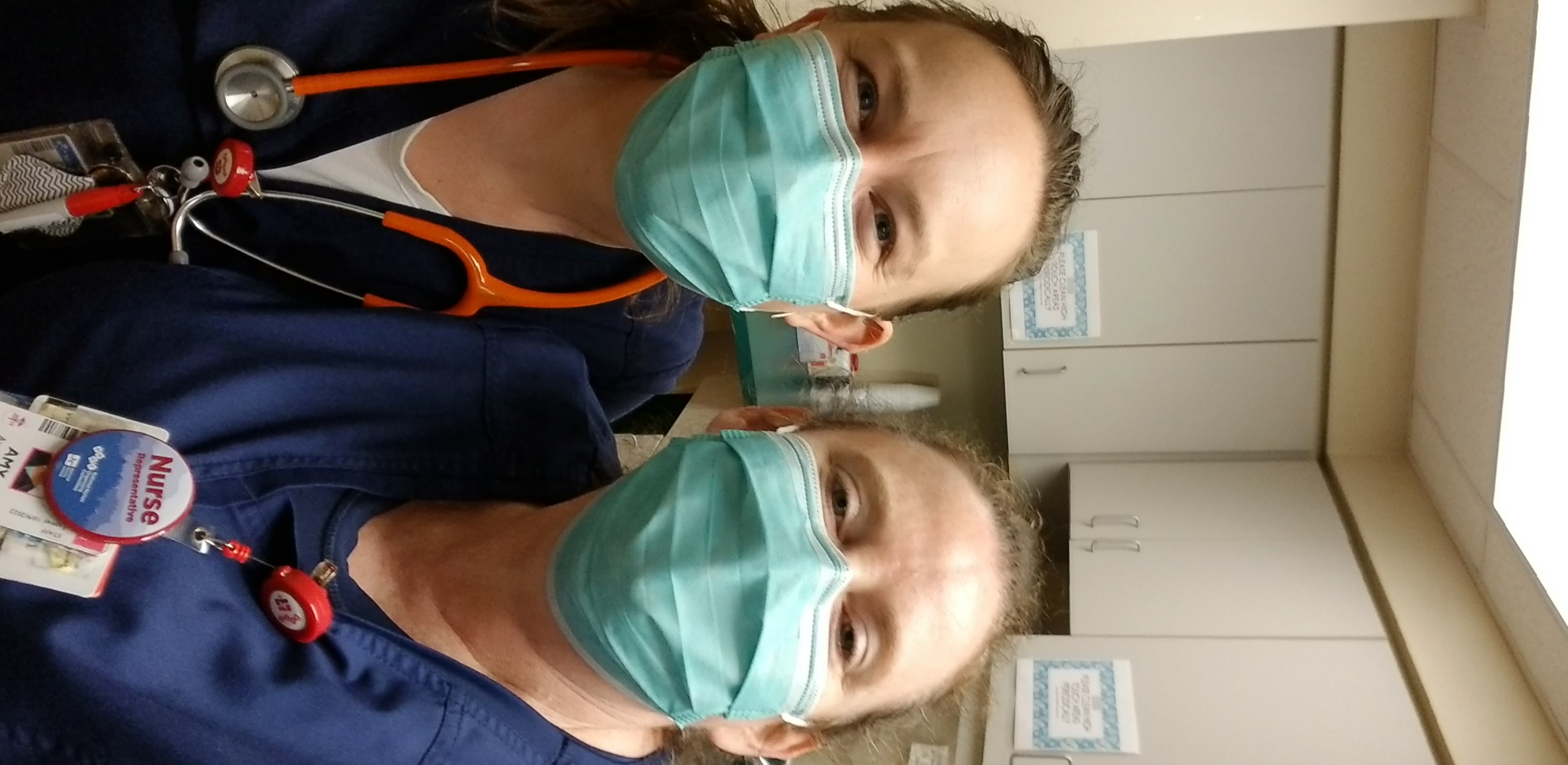 Amy Waters is pictured on the left with another nurse to her right. They are taking a selfie photo with masks and scrubs.