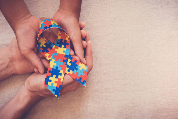Two sets of hands holding an Autism Awareness Ribbon made of several colorful puzzle pieces
