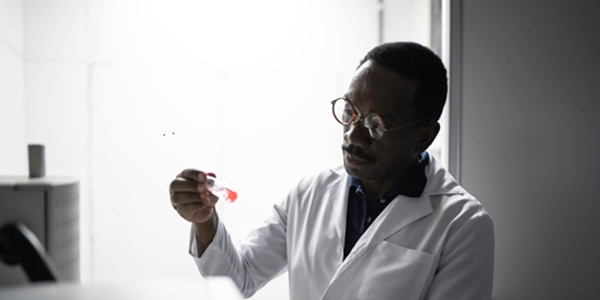 A Black scientist in a white lab coat examines a test tube